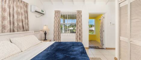 A bedroom with a bed, curtains, an air conditioning unit, and a view through a window.