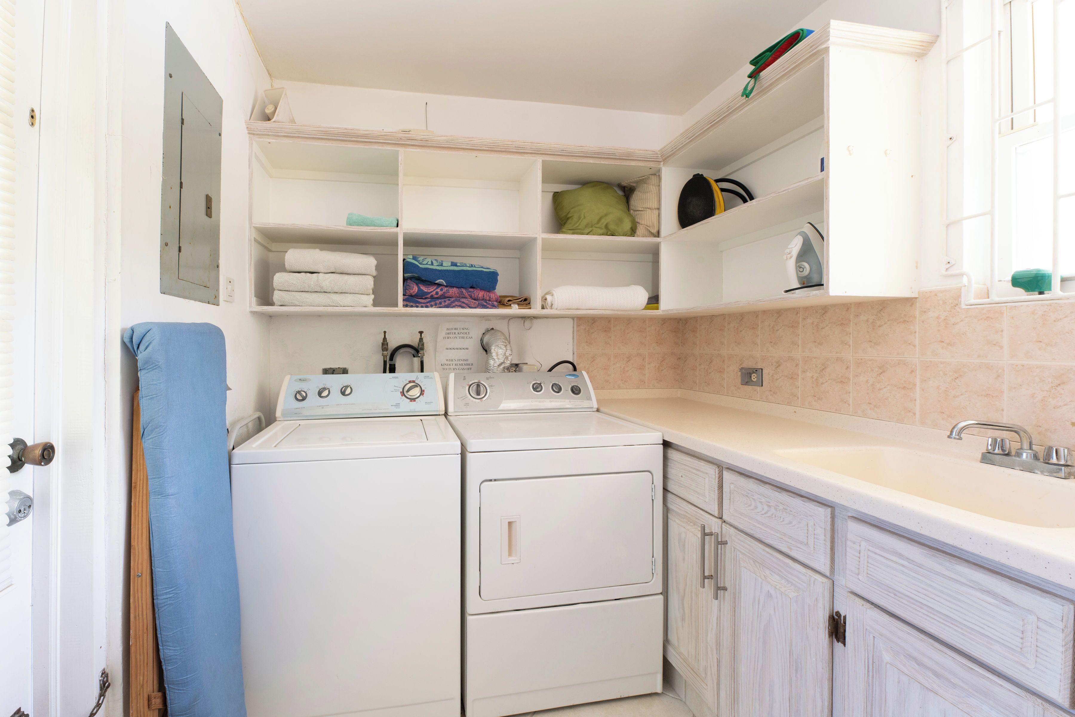 A laundry area with two white washing machines, a sink, and a countertop.