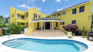 A yellow building with a swimming pool, steps leading to a covered area, and outdoor furniture. - Vida Mejor West Pool (Private Pool) (Holetown)
