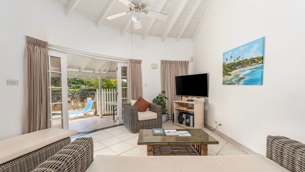 A living room with a TV, wicker furniture, and a painting of a beach. - Vida Mejor--Waterfall (Private Pool) (Holetown)