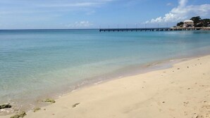 A beach with clear water, a pier extending into the sea, and buildings on the shore. - Vida Mejor--Waterfall (Private Pool) (Holetown)