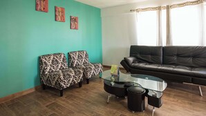 A living room with teal walls, a black leather sofa, patterned armchairs, and a glass coffee table. - Emerald One Bedroom Suite (Ocho Rios)