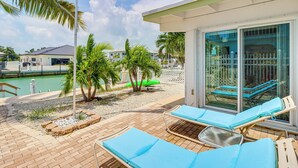 A poolside area with lounge chairs, palm trees, and a glass-enclosed patio. - Waterfront Colony Beach Duplex! w/ Golf Cart! (Key Colony Beach)