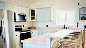 A kitchen with white cabinets, stainless steel appliances, and a wooden island with seating. - 3-bedroom 2 bath cottage-Walk to beach or golf
Course.Hot Tub and outside shower (Kitty Hawk)