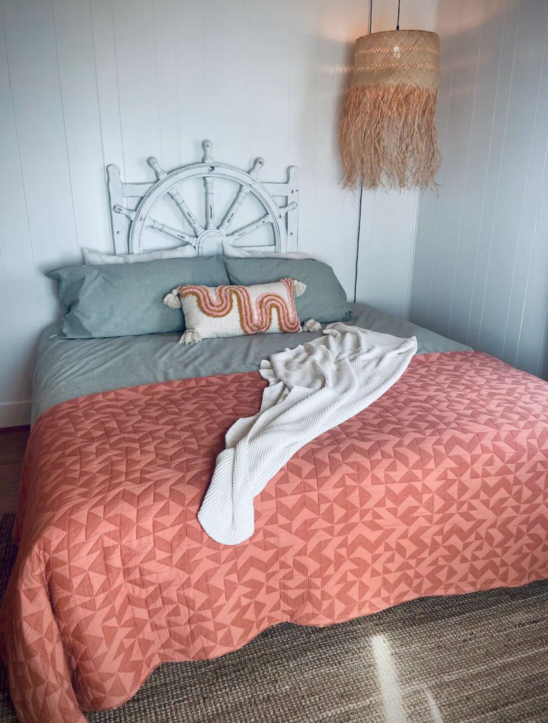 A bed with a geometric patterned bedspread, a white throw blanket, and a decorative headboard.