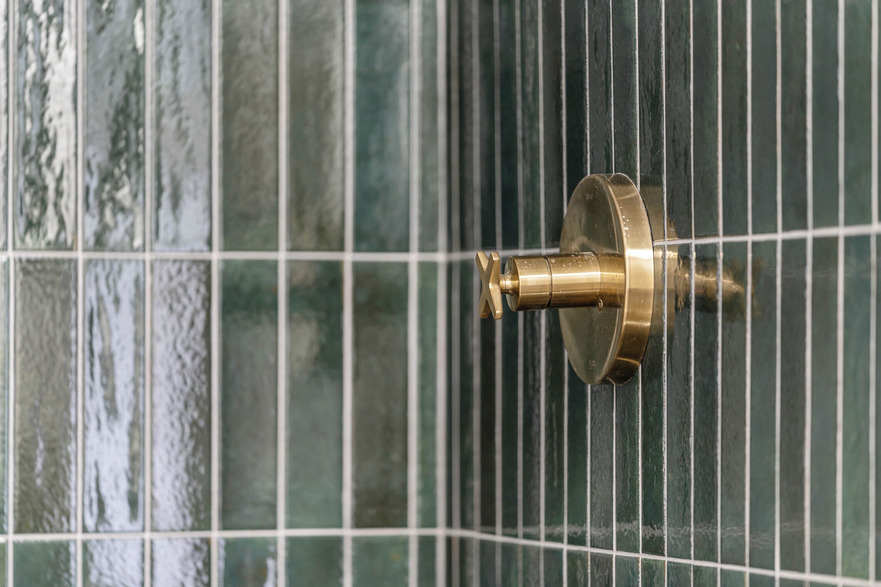 A brass shower knob on a tiled wall.