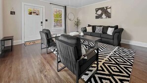 Ein Wohnzimmer mit einer Couch, Sesseln, einem Couchtisch, einem gemusterten Teppich und einer Tür.
