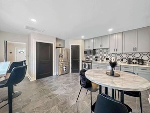 A modern kitchen with grey cabinets, a stainless steel refrigerator, a round marble table, and a dining area with black chairs. - Black and white chic retreat (Charlotte)