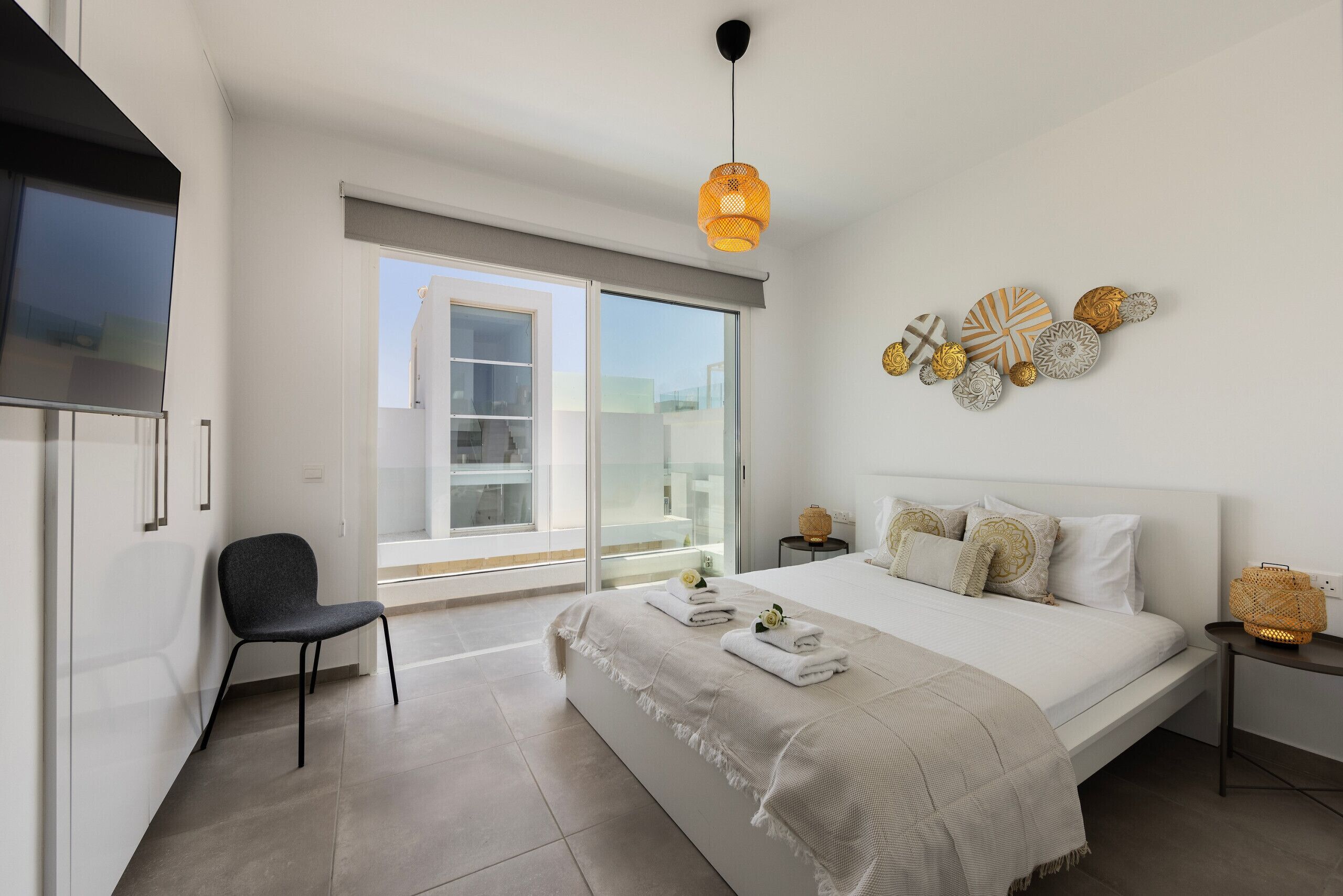 Ein modernes Schlafzimmer mit einem großen Bett, einem Sessel, einem Nachttisch, einer Wanddekoration und einem Fenster mit Blick.
