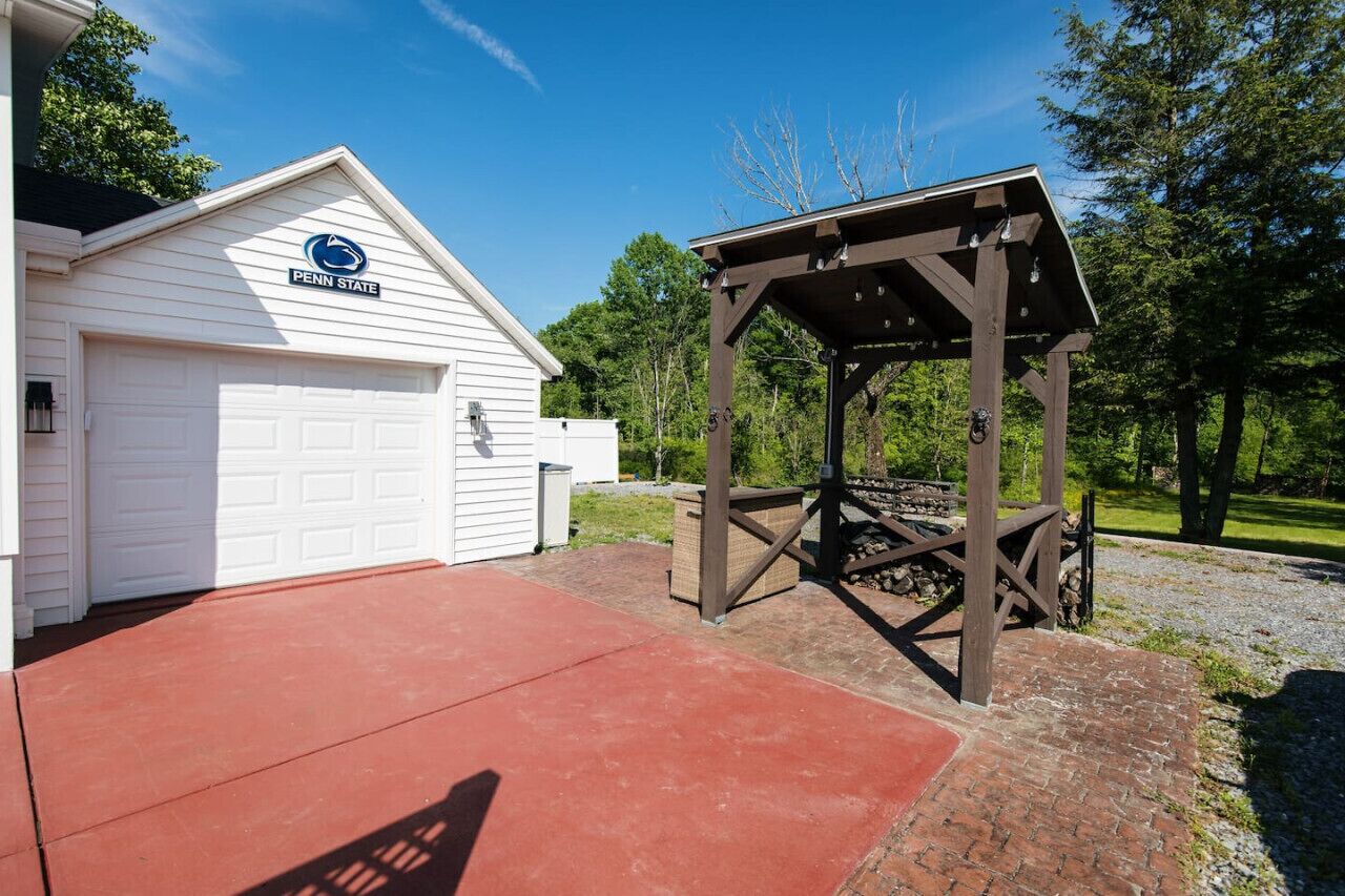 A white garage with a 'Penn State' sign, a wooden gazebo, and a red concrete driveway.