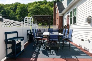 Une terrasse extérieure avec une table et des chaises, un espace salon abrité et une clôture blanche.