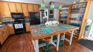 A kitchen with wooden cabinets, a black refrigerator, a microwave, and a stove. There is a table with green stools and a decorative centerpiece.