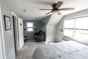 Une chambre à coucher avec un lit, un ventilateur de plafond, une fenêtre, une chaise et un radiateur.