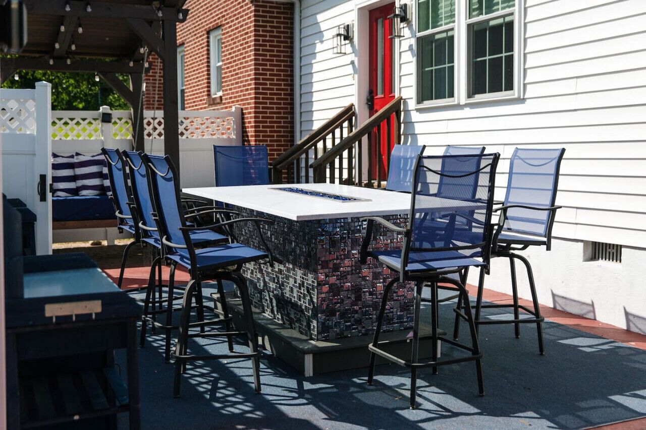 An outdoor patio with a table and chairs, a brick wall, and a white building with a red door in the background.