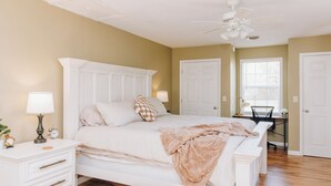 A bedroom with a bed, bedside tables, a desk, and a ceiling fan.