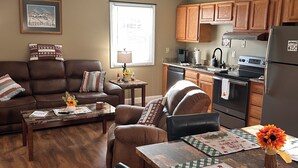 A cozy living room with a brown leather couch, a dining table with a floral centerpiece, and wooden flooring.