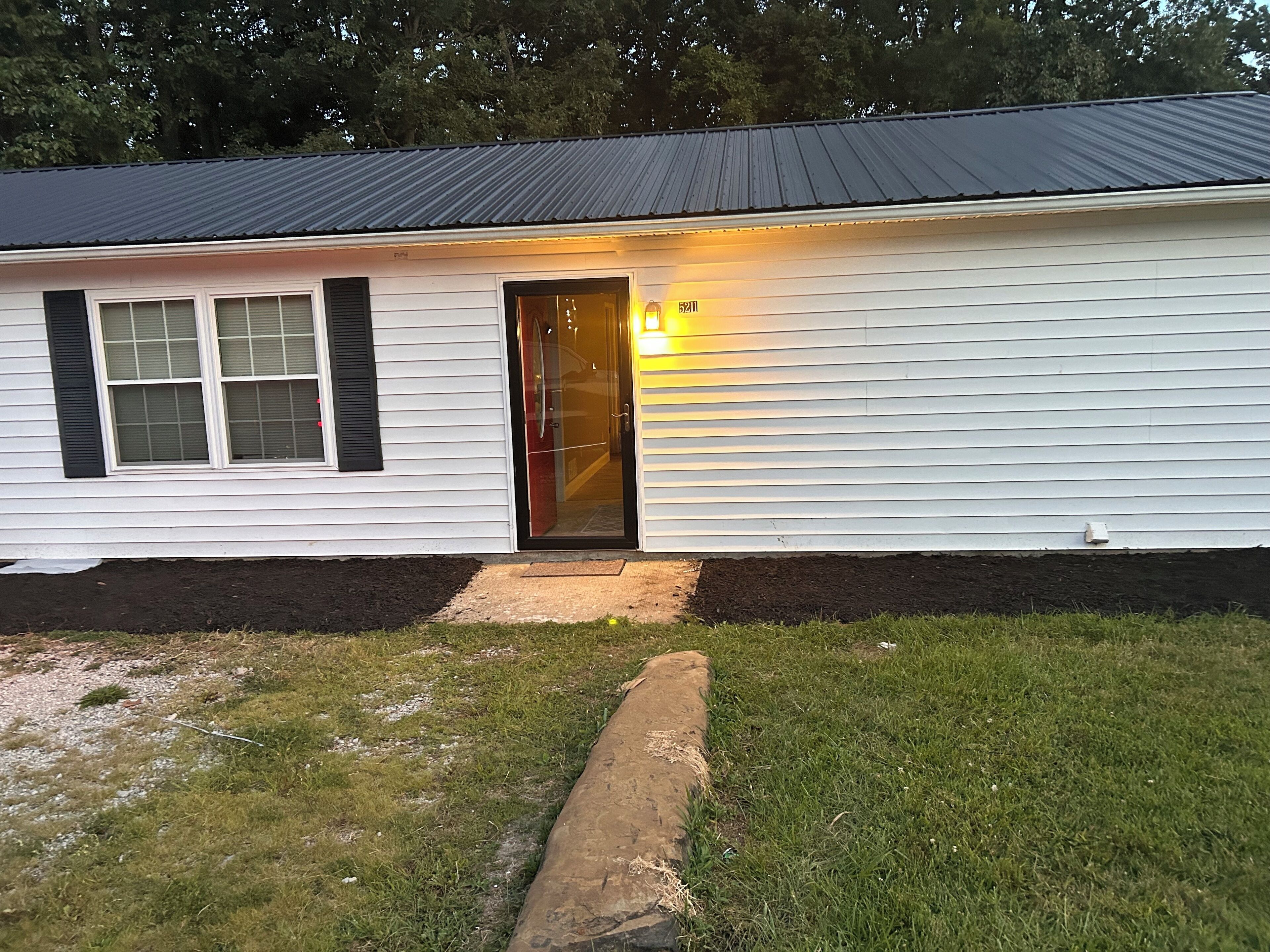 A single-story house with a dark roof, white siding, and a front door with a small porch.