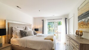 A bedroom with a large bed, a nightstand, a dresser, and a view of the outdoors.