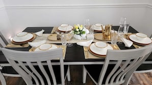 A dining table set with white chairs, gold-rimmed plates, and clear glassware.