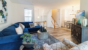 A spacious living room with a blue sofa, a round coffee table, and a staircase leading to another level.
