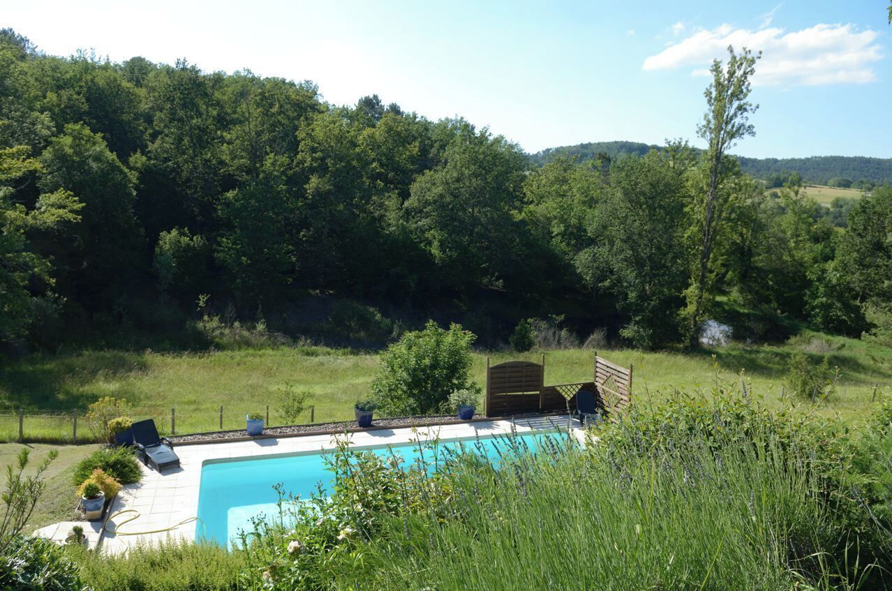 A swimming pool with a wooden deck, surrounded by lush greenery and hills in the background.