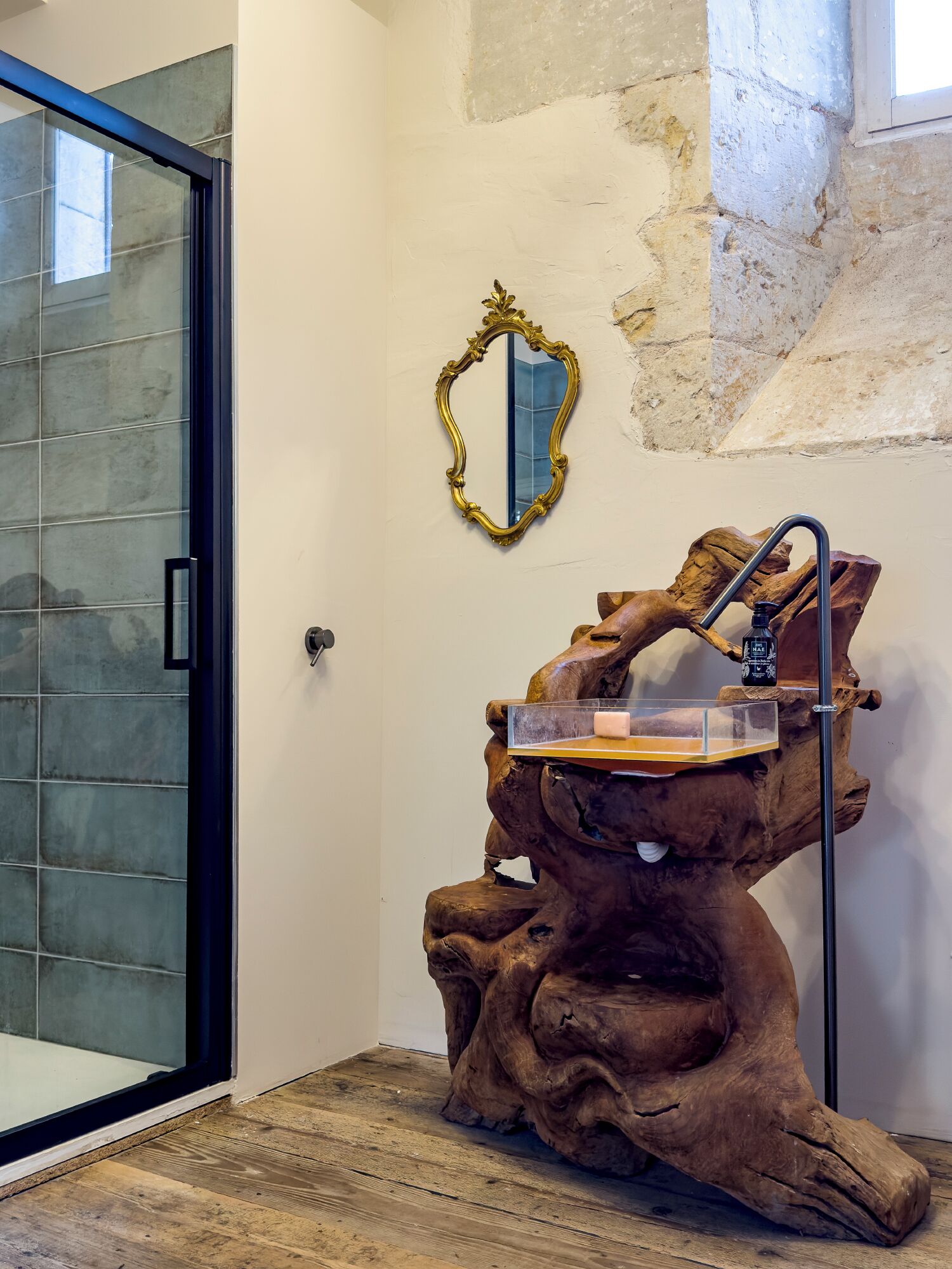 A bathroom with a glass shower enclosure, a wooden tree trunk sink, and a gold-framed mirror.