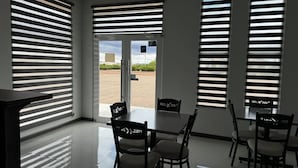 A hotel room with a dining area, large windows with blinds, and a view of the outdoors. - REL-X INN (Ahumada)