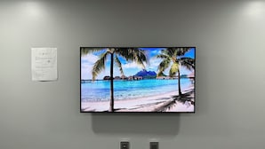 A flat-screen TV mounted on a wall displaying a tropical beach scene. - REL-X INN (Ahumada)