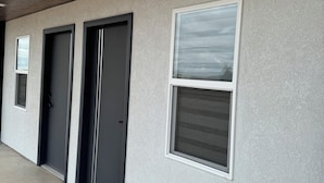 A building exterior with three doors and two windows, a concrete floor, and a textured wall. - REL-X INN (Ahumada)