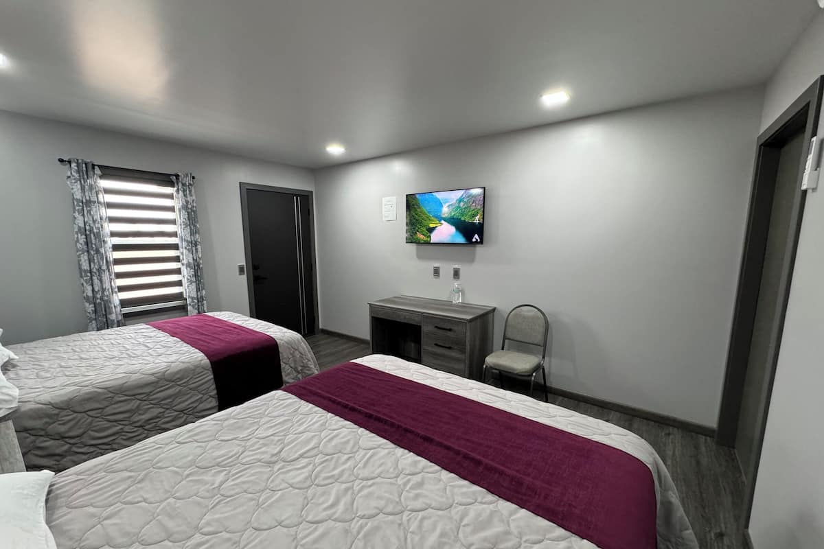 Une chambre d’hôtel avec deux lits, un bureau, une chaise, une télévision et une fenêtre avec des rideaux.