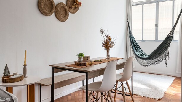 A modern living room with a wooden herringbone floor, a white wall with woven baskets, a hammock, and a dining area with a table and chairs. - 3 minutes from Leme beach | GS501 (Rio de Janeiro)