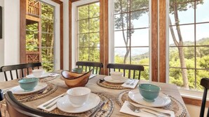 A dining table set with plates, bowls, and cutlery, surrounded by large windows with a view of trees and hills. - The Camp - Luxe Blue Ridge Condo (Burnsville)