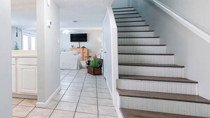 A staircase leading to a landing with a flat surface, a white wall with a flat-screen TV mounted above a wooden cabinet, and a potted plant on the landing. - 3 Bedroom Townhouse, Access to 4 pools, hot tub, & a 5 minute walk to white sand (Panama City Beach)