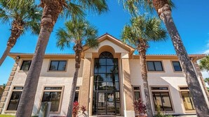 A building with a central entrance, flanked by palm trees, and a clear blue sky. - 3 Bedroom Townhouse, Access to 4 pools, hot tub, & a 5 minute walk to white sand (Panama City Beach)