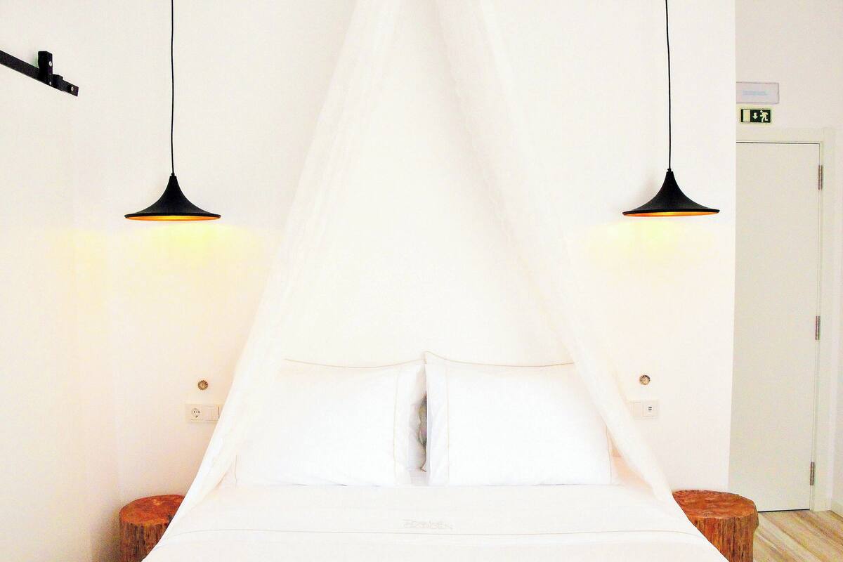 A bed with white bedding, two pendant lights, and a white door in the background.