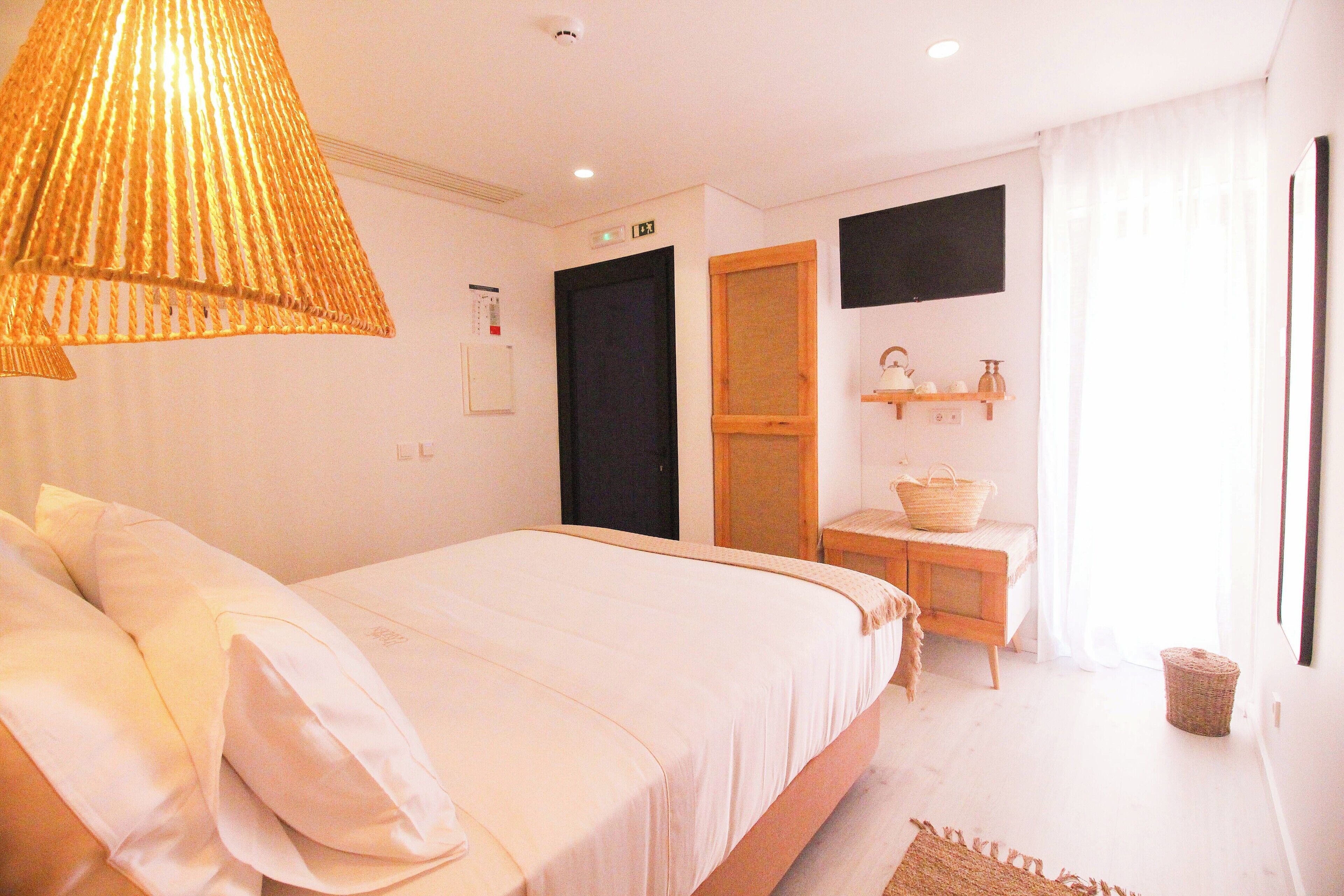 A bedroom with a bed, a wooden desk, a chair, a hanging lamp, and a window with curtains.