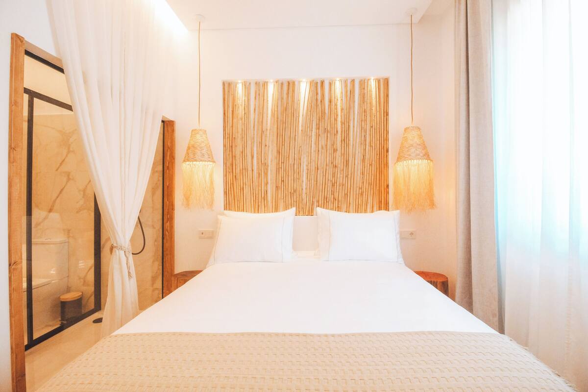 A hotel room with a large bed, two bedside lamps, a wooden headboard, and a large mirror.