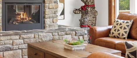 A stone fireplace with a fire, a bear sculpture, leather sofas, and a wooden coffee table.