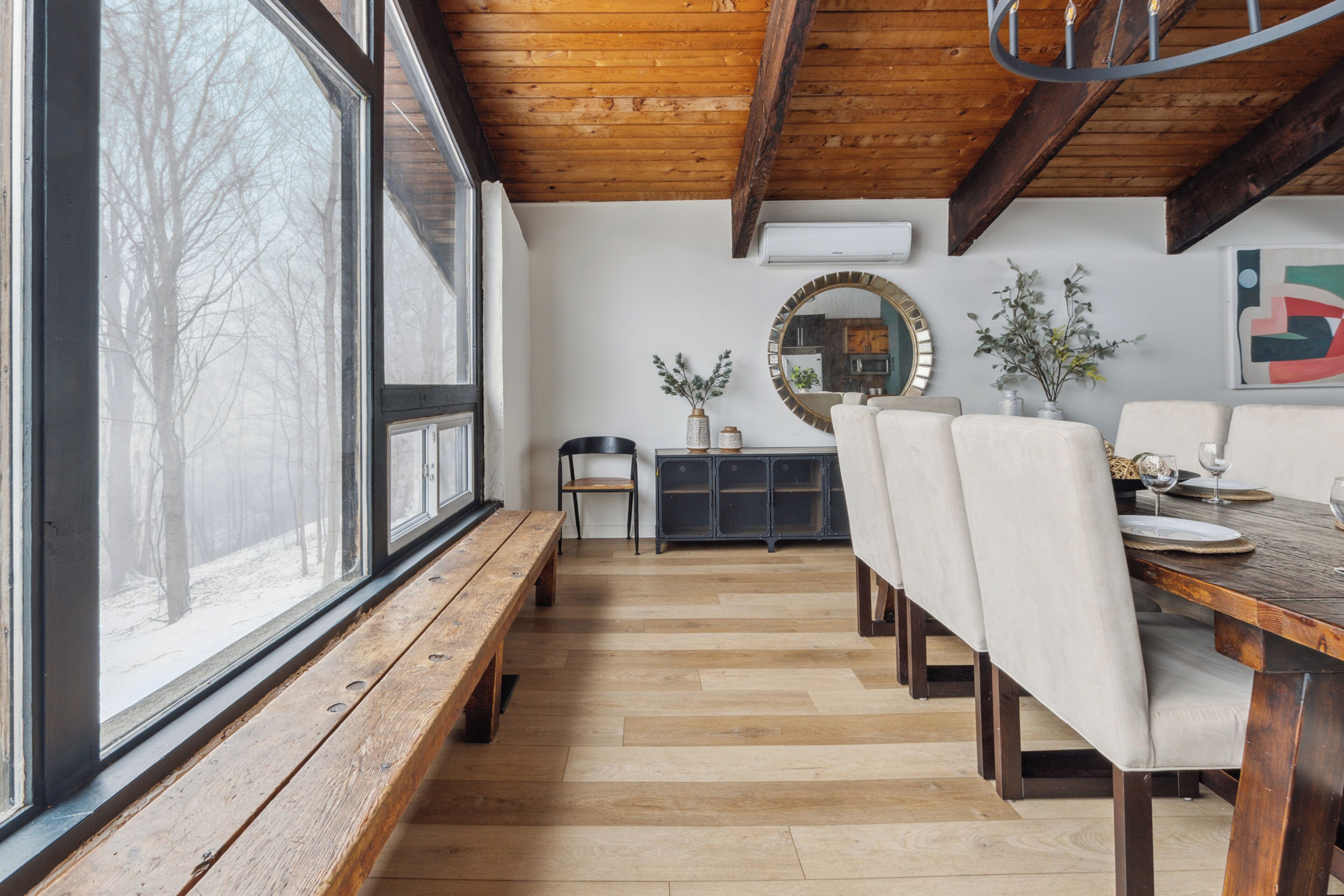A dining area with a wooden bench, a dining table with chairs, and a view through large windows.