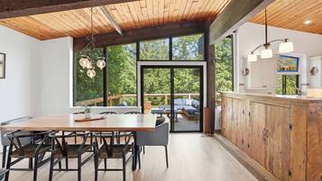 A modern kitchen with a wooden countertop, a dining area with a table and chairs, and large windows offering a view of the outdoors.