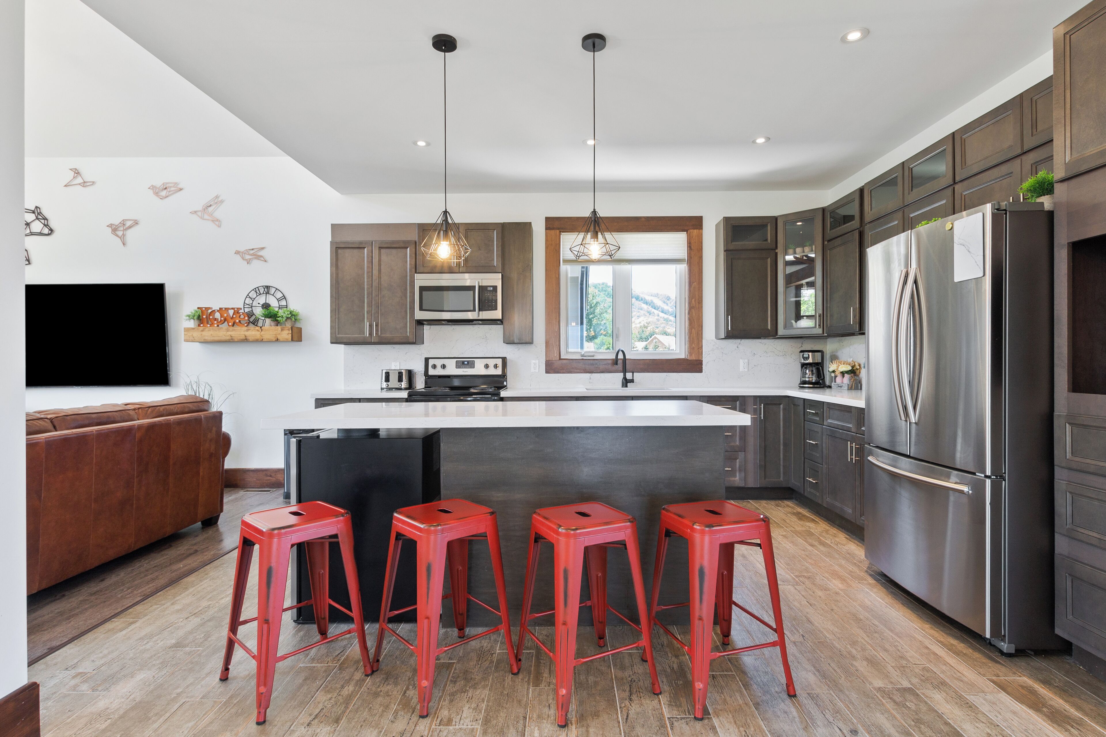 A modern kitchen with a central island, stainless steel appliances, and a brown leather couch.