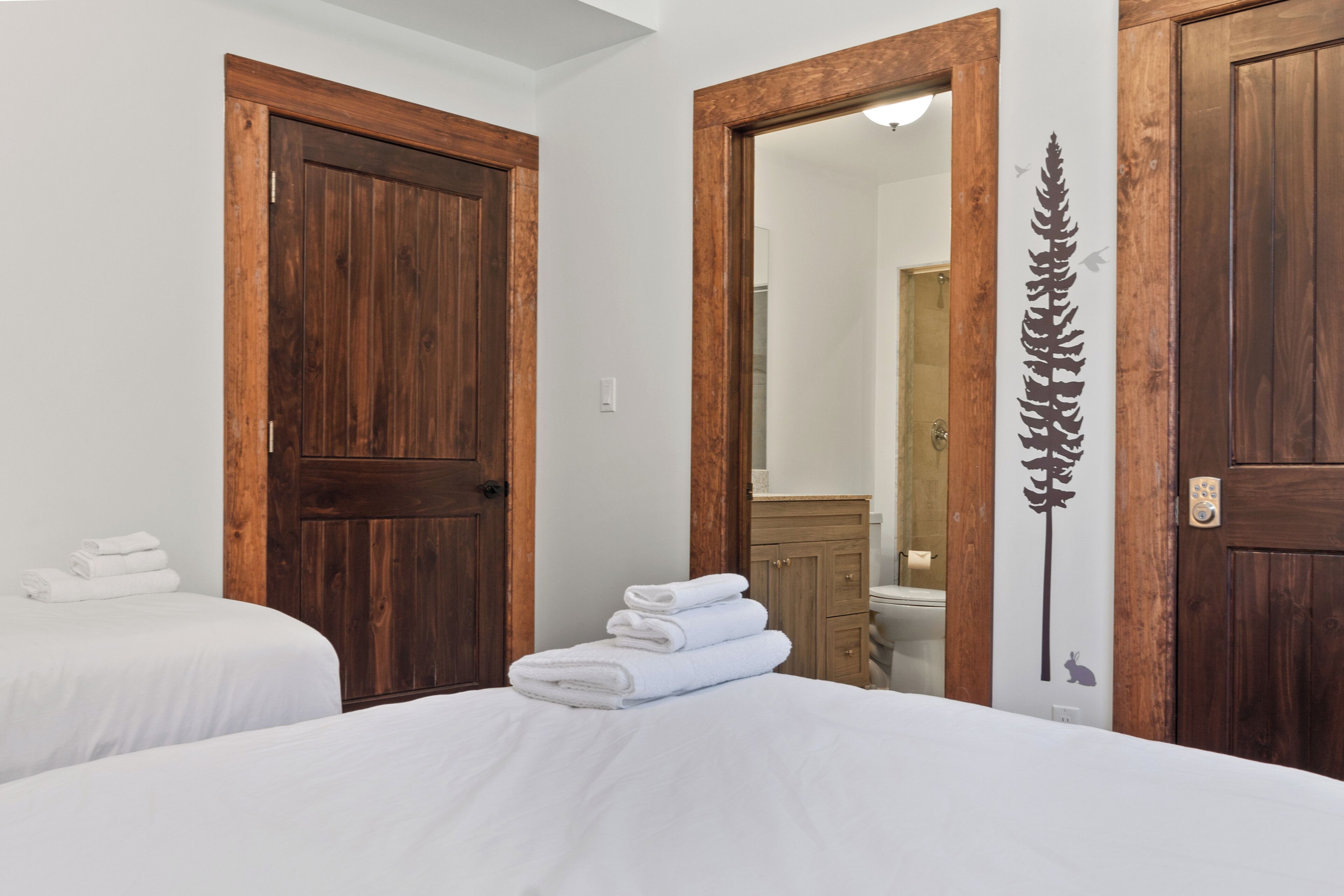 A hotel room with two beds, wooden doors, a mirror, and a decorative wall piece.
