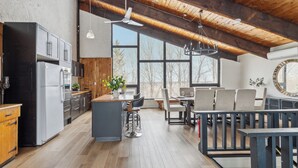 Une cuisine spacieuse dotée d’appareils modernes, d’un plafond en bois et de grandes fenêtres offrant une vue sur l’extérieur.