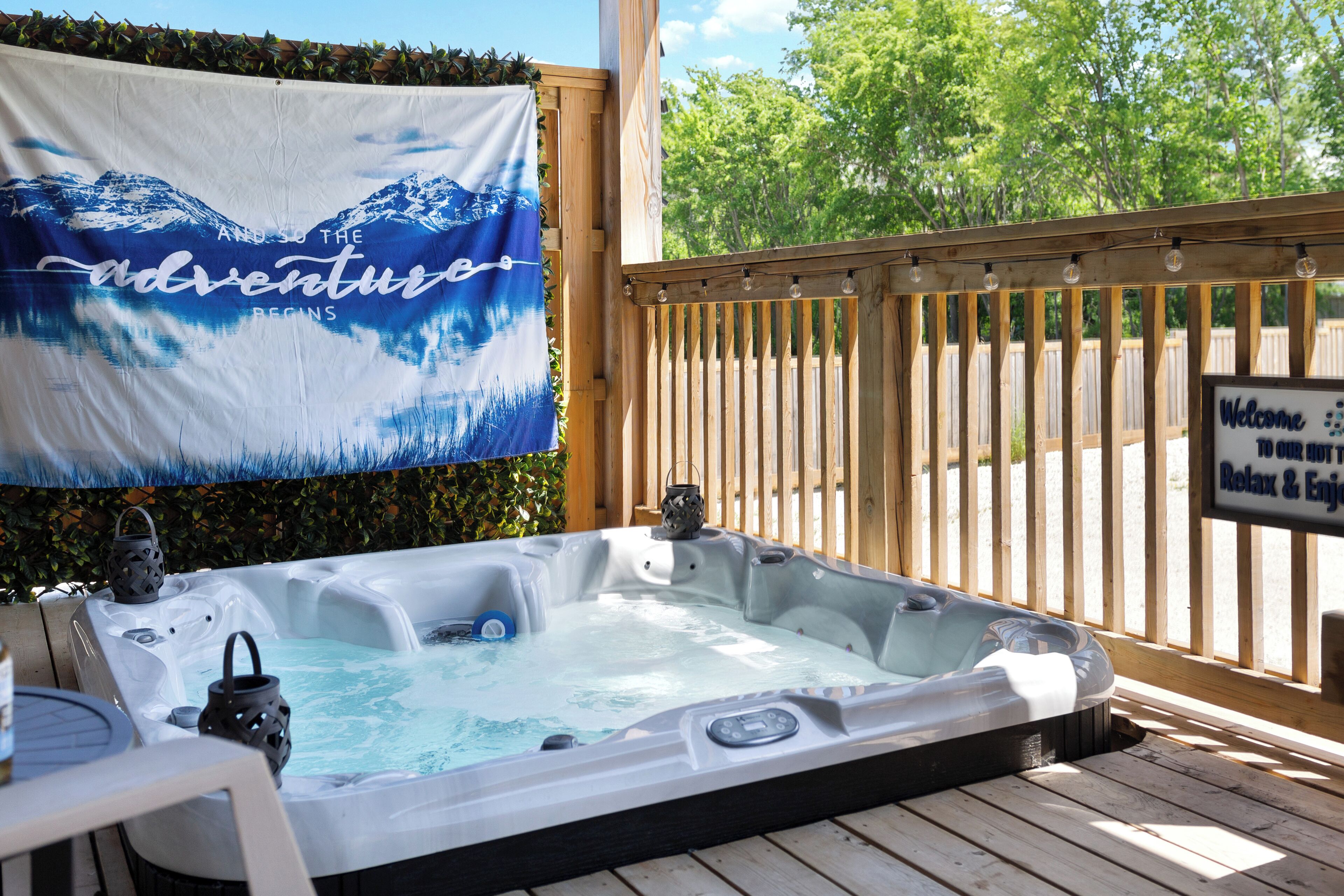 Un bain à remous sur une terrasse en bois, avec une banderole sur laquelle on peut lire « l’aventure commence » et un panneau d’accueil.