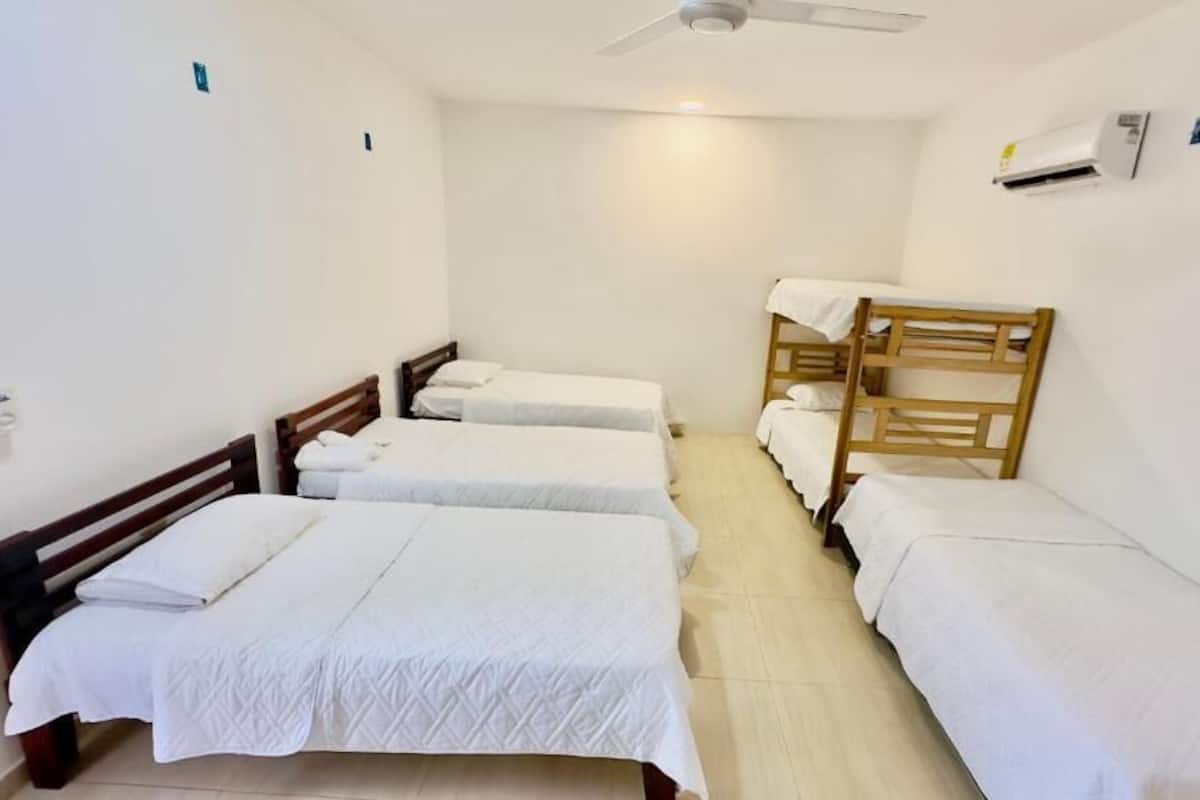 Habitación tipo dormitorio con cuatro camas individuales, ventilador de techo y aire acondicionado.