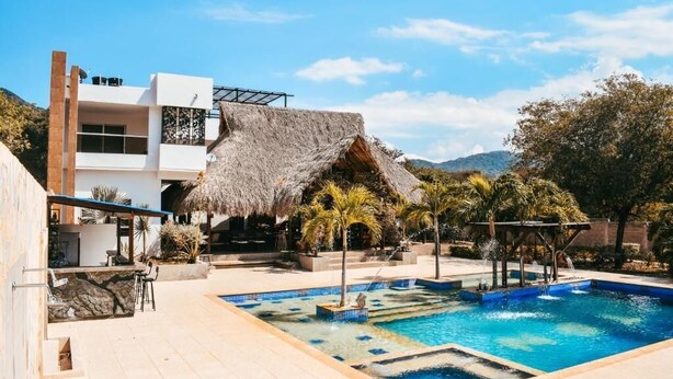 A modern hotel with a pool, a bar area, and a thatched-roof structure. - Hotel boutique Rancho ton (Santa Marta)