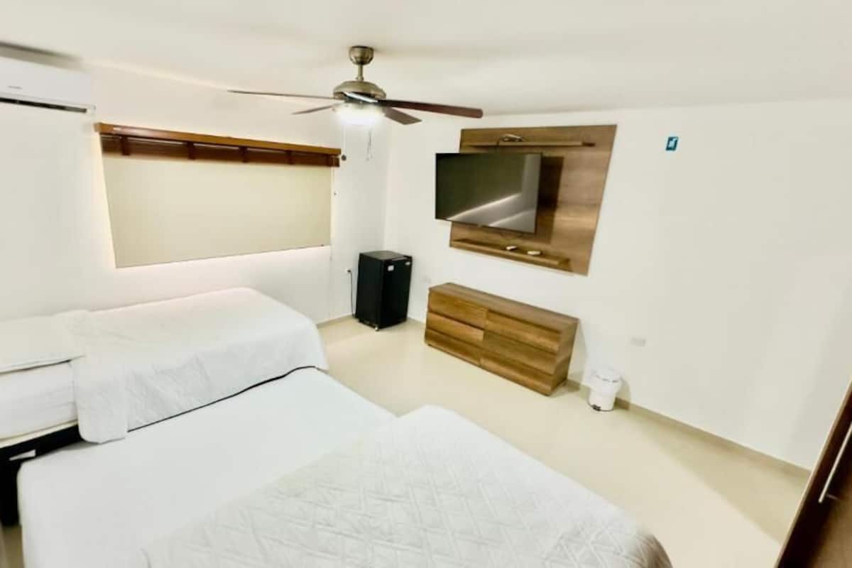 Habitación de hotel con dos camas, televisión, ventilador de techo y cómoda de madera.