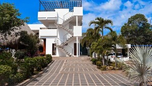 A modern building with a central staircase, surrounded by tropical vegetation and a paved walkway. - Hotel boutique Rancho ton (Santa Marta)