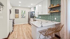 A modern kitchen with white cabinets, a marble island, and a green tiled backsplash. - Downtown Zen - Central Location in Centerville, OH (Centerville)