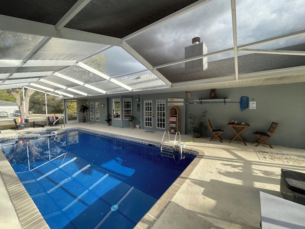 A covered swimming pool with a glass ceiling, lounge chairs, and potted plants.